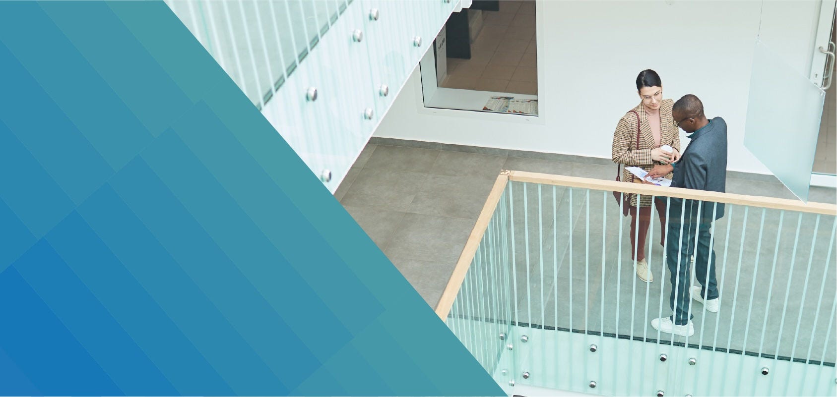 Two people in business attire discuss a project on an indoor office balcony